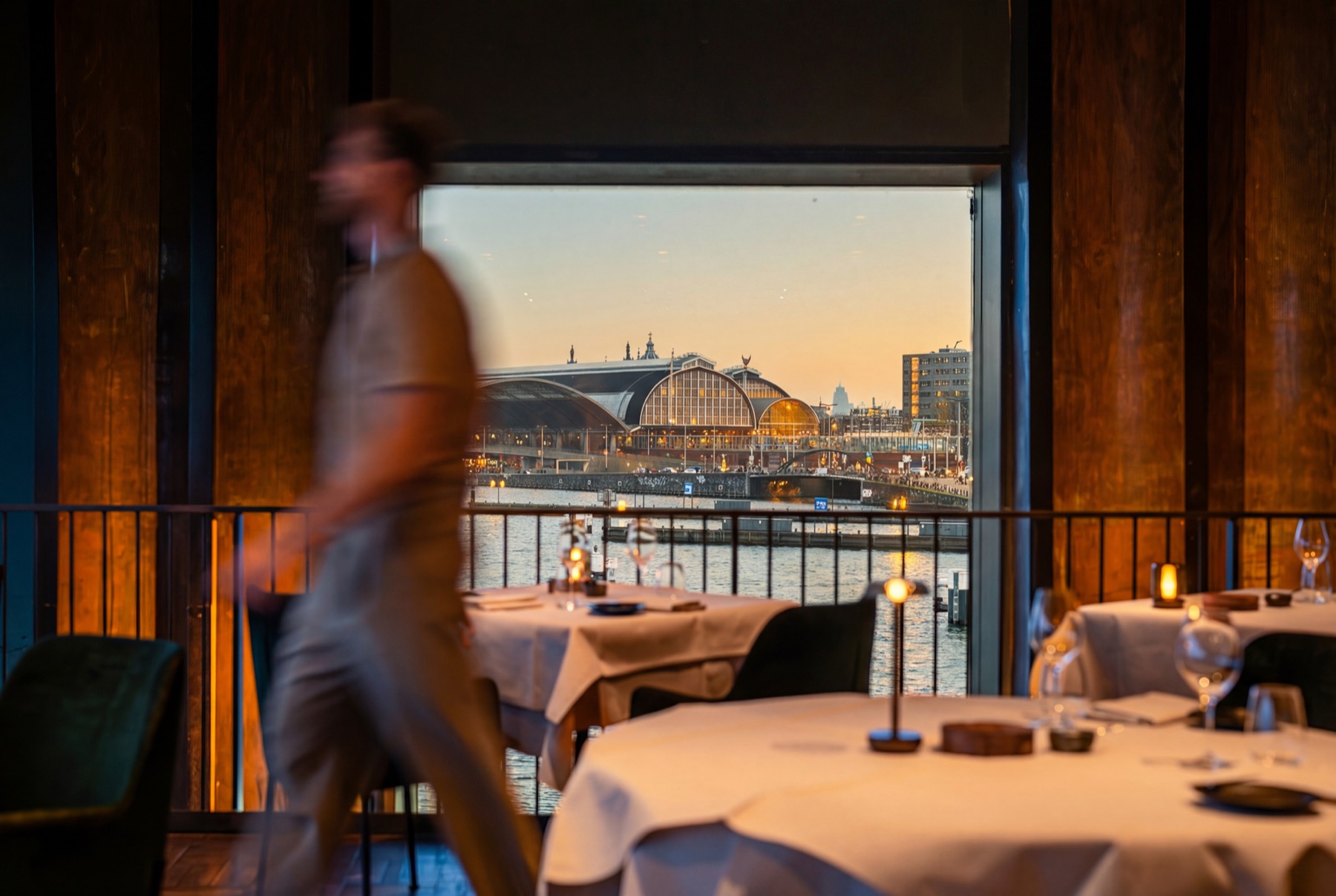 De eetzaal van MOS met gedekte tafels en uitzicht over het IJ op Amsterdam Centraal