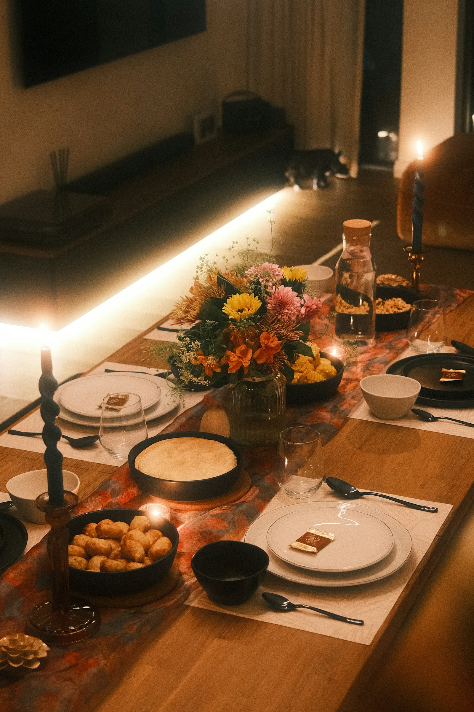 Een gedekte tafel bij kaarslicht, met borden, bloemen en brandende kaarsen
